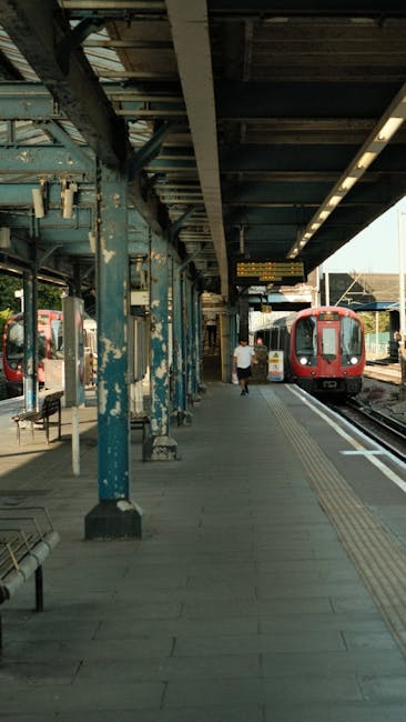 A photograph of an outdoor railway station platform captures a wooden and concrete surface with a textured tactile paving strip along the edge for safety. The platform features blue-painted metal supp